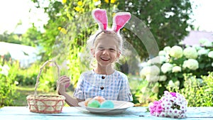 a little girl with bunny ears dyes Easter eggs in nature and smiles, a cute child is engaged in creativity
