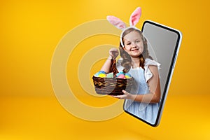 A little girl in bunny ears holds a basket with colorful Easter eggs and looks out of a smartphone.