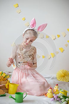 Little girl with bunny ears painting eggs, Easter decoration