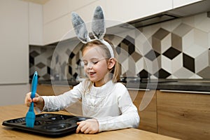 Little girl in bunny ears smiling and lubricate baking dish with silicone brush