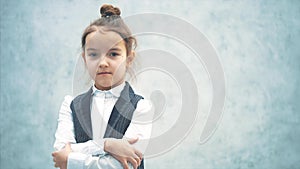 The little girl business lady stands on a gray background. During this, he looks closely at the camera. Puts a hand on