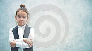 The little girl business lady stands on a gray background. During this he takes a look at the camera. Puts a hand on his