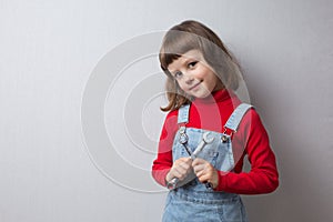 A little girl in a car mechanic uniform is holding wrenches