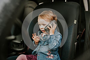 Little girl in a car seat. Holding phone in her hand. Taking driver seat. Car damage. Authentic image