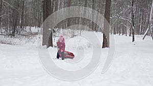 A little girl carries a tube downhill in the snow in winter. Tubing, family outdoor activities