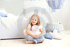 A little girl in casual clothes holds a cloud pillow against the background of a decorative balloon. The child plays in children r