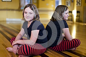 Little girl in casual clothes sitting cross-legged on the floor of a danse studio