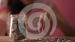 Little girl in casual dress putting money into a glass jar for future costs.