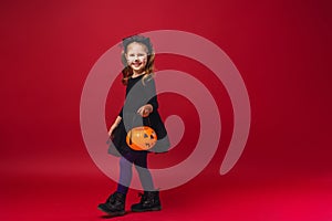 Little girl in cat costume with mustache and ears, with pumpkin in her hands