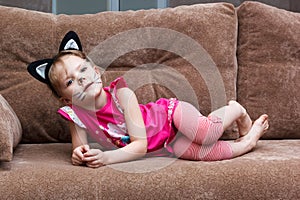 Little girl with cat face painting on couch