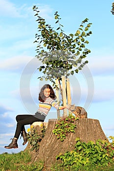 Little girl  with cat sitting on stump by new linden
