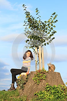 Little girl  with cat sitting on stump by new linden