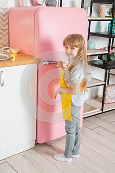 A little girl of Caucasian appearance, 7 years old, opens the door of pink frige