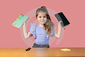 A little girl caught in a school desk holding two books showing interesting emotions, the girl loves to read books and