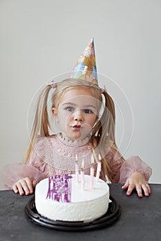 Little girl celebrating birthday party. Blond with long hair ponytails Child blows candles on birthday cake