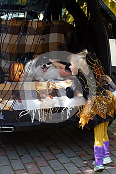 Little girl celebrating Halloween pet dog car trunk. Fun outdoors