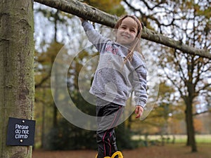 Little girl cheeky smile climbs tree with sign saying please do not climb
