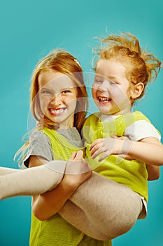 Little girl cheerfully throws younger sister in her arms, expresses sincere joyful emotions, two relatives on blue