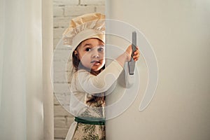 Little girl in a chef hat looks into the refrigerator