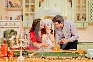 a little girl in a chef& x27;s cap with mom and dad decorates a gingerbread house