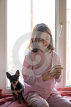 Little girl with a chihuahua. Little girl with a smartphone in her hands. Teenager at home with an animal