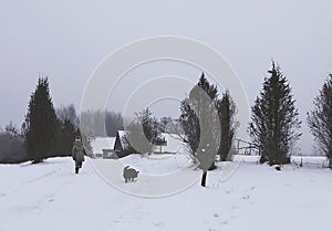 Little girl child in a beige coat running with small balck dog on snow covered field in the village