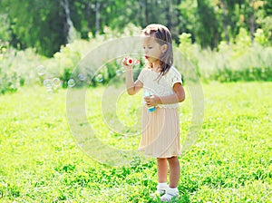 Little girl child blowing soap bubbles in summer