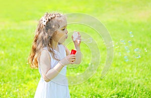 Little girl child blowing soap bubbles in summer sunny