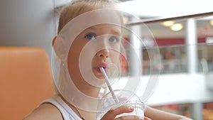 Little girl child in cafe drinking milk cocktail cacao with milk. Child drinks a milkshake sits in a cafe.