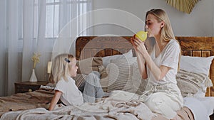 Little girl child daughter baby kid sitting with loving mother babysitter on bed in cozy bedroom play looks how mom