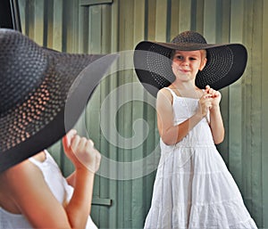 A little girl child fashionista stands in front of the mirror and admires her reflection. A girl in a white dress