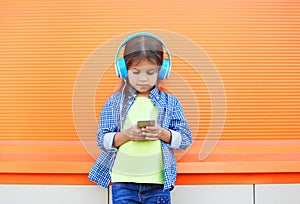 Little girl child listens to music in headphones and using smartphone