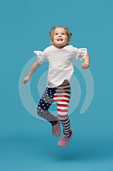Little girl child in patriotic american pants jumping for joy on a blue