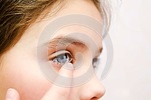 Little girl child putting contact lens into her eye closeup