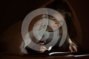 Little girl child read book in bed under the covers at night