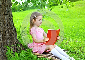 Little girl child reading a book on the grass near tree