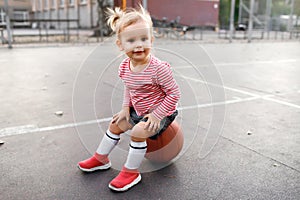 Little girl child sits on a basketball ball and looks attentively and smiles