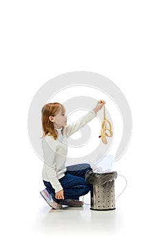 Little girl, child taking away garbage, throwing banana peel into trash bin isolated over white background