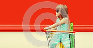 Little girl child with trolley cart and shopping bags on city street