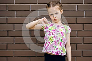 Little girl child is unhappy and shows a thumb down gesture