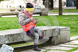 Little girl child using a mobile phone in public park.