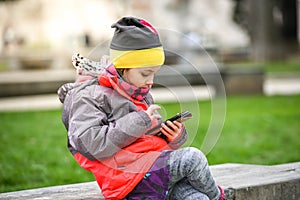 Little girl child using a mobile phone in public park.