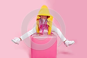 Little girl child in white jeans, colored clothes sitting with raised legs on a chair in the studio, on pink background