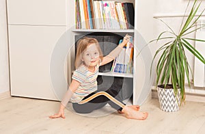 Little girl chooses a book in a bookcase at home.