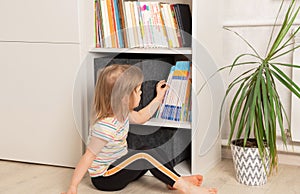 Little girl chooses a book in a bookcase at home.