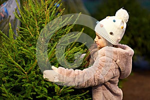 Little girl choosing christmas tree at market