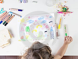 Little girl choosing a green coloured pencil in a wood table for