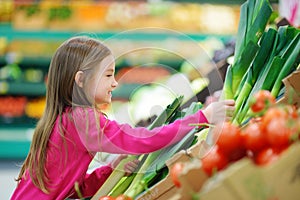 Little girl choosing a leek in a food store or supermarket