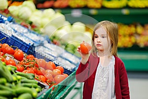 Little girl choosing tomatoes in a food store