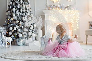 A little girl with a christmas gift with christmas tree and lights  background. Holiday concept.